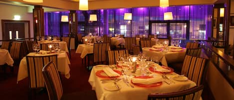 A restaurant with multiple tables set for dining, featuring white tablecloths and striped chairs.