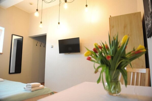 A hotel room with a bed, a flat-screen TV mounted on the wall, a mirror, and a vase with tulips on the table. - Dom Casimi (Kraków)