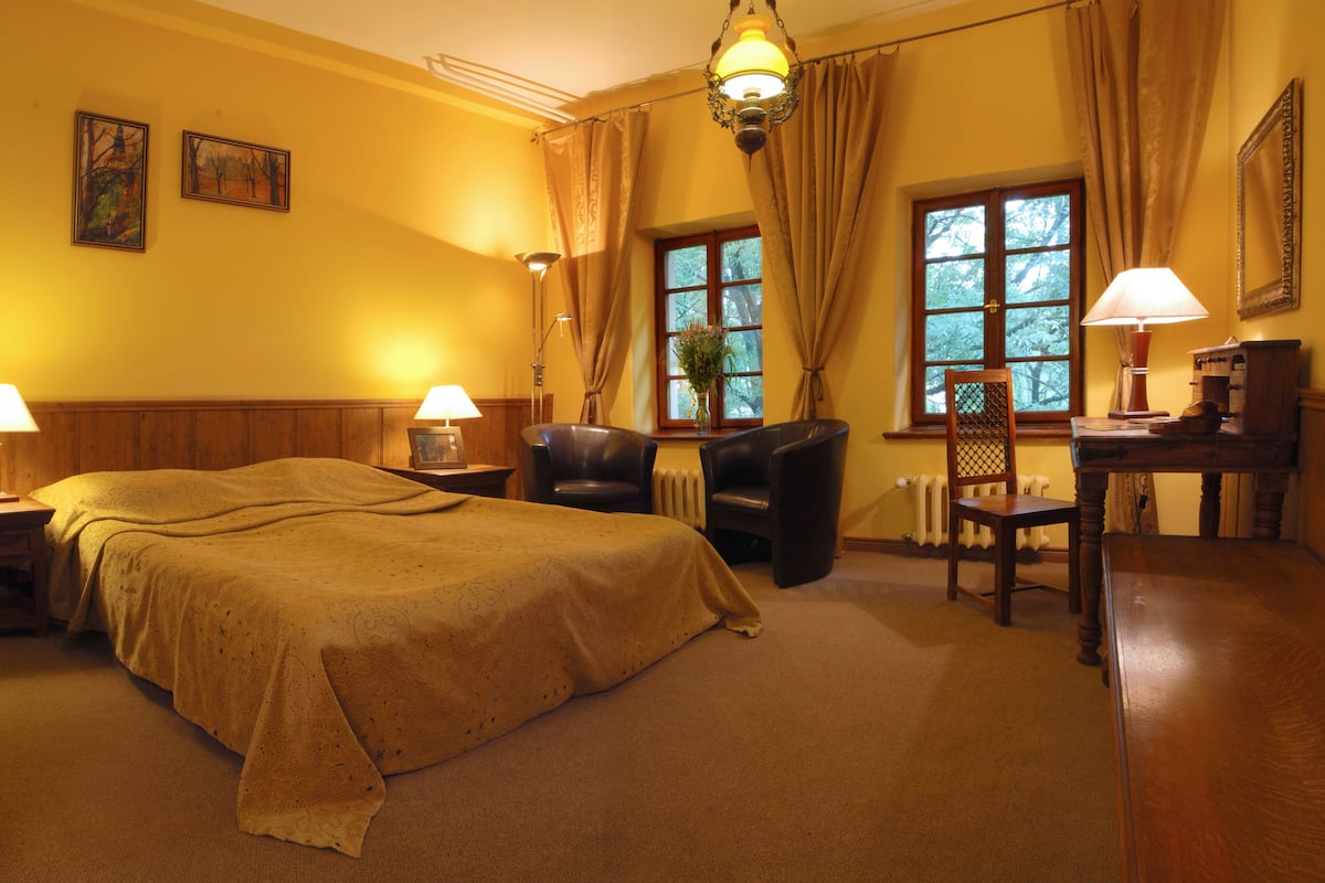 Habitación de hotel con una cama grande, dos sillas, un escritorio con lámpara y una ventana con cortinas.