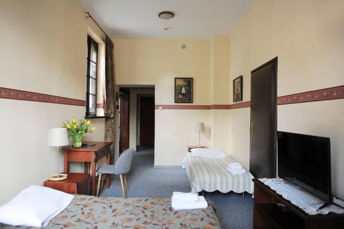 Habitación de hotel con dos camas, un escritorio con lámpara, televisión y ventana con cortinas.