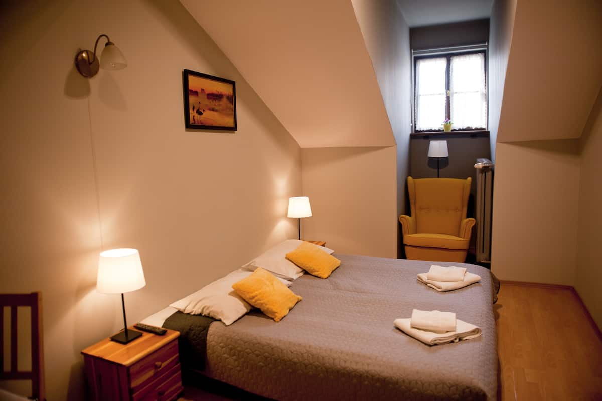 Un dormitorio con una cama, dos lámparas de noche, una silla, una mesita de noche y una ventana.