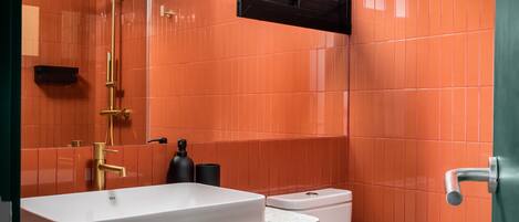 Un bagno con un lavandino bianco, una doccetta dorata e piastrelle arancioni.