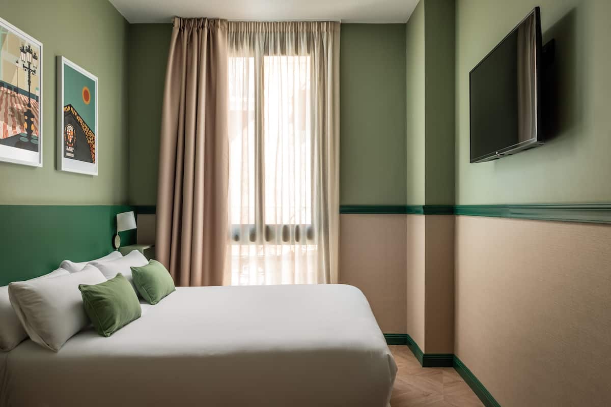 A hotel room with a bed, curtains, a TV, and two framed pictures on the wall.