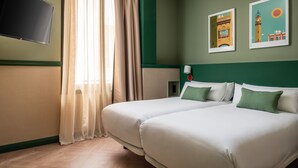 Une chambre d’hôtel avec deux lits, un téléviseur à écran plat, une fenêtre avec des rideaux et deux tableaux encadrés accrochés au mur.