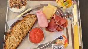 Un plateau repas comprenant un croissant, du café, des fruits, du fromage, du jambon, du pain et des condiments.