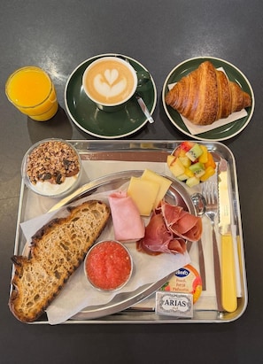 A meal tray with croissant, coffee, fruit, cheese, ham, bread, and condiments. - BYPILLOW Twenty (Barcelona)