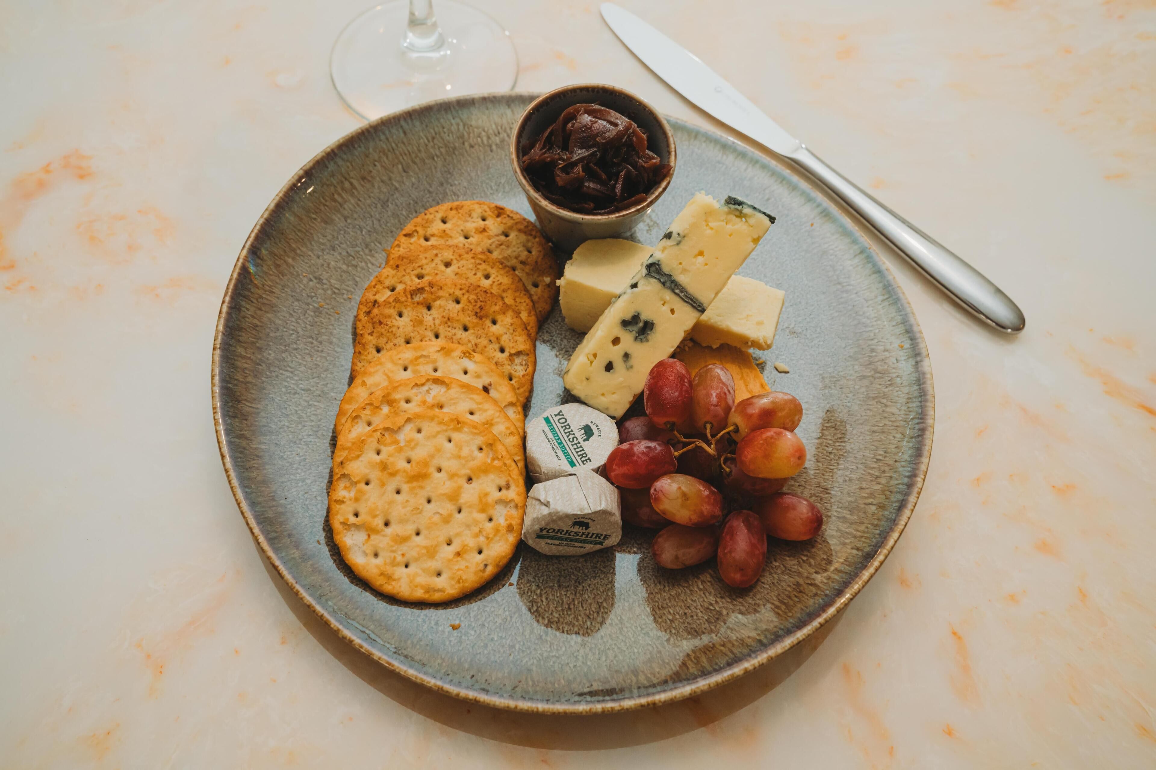 Ein Teller mit Crackern, Käse, Trauben und einer kleinen Schale Schokolade auf einem Tisch.