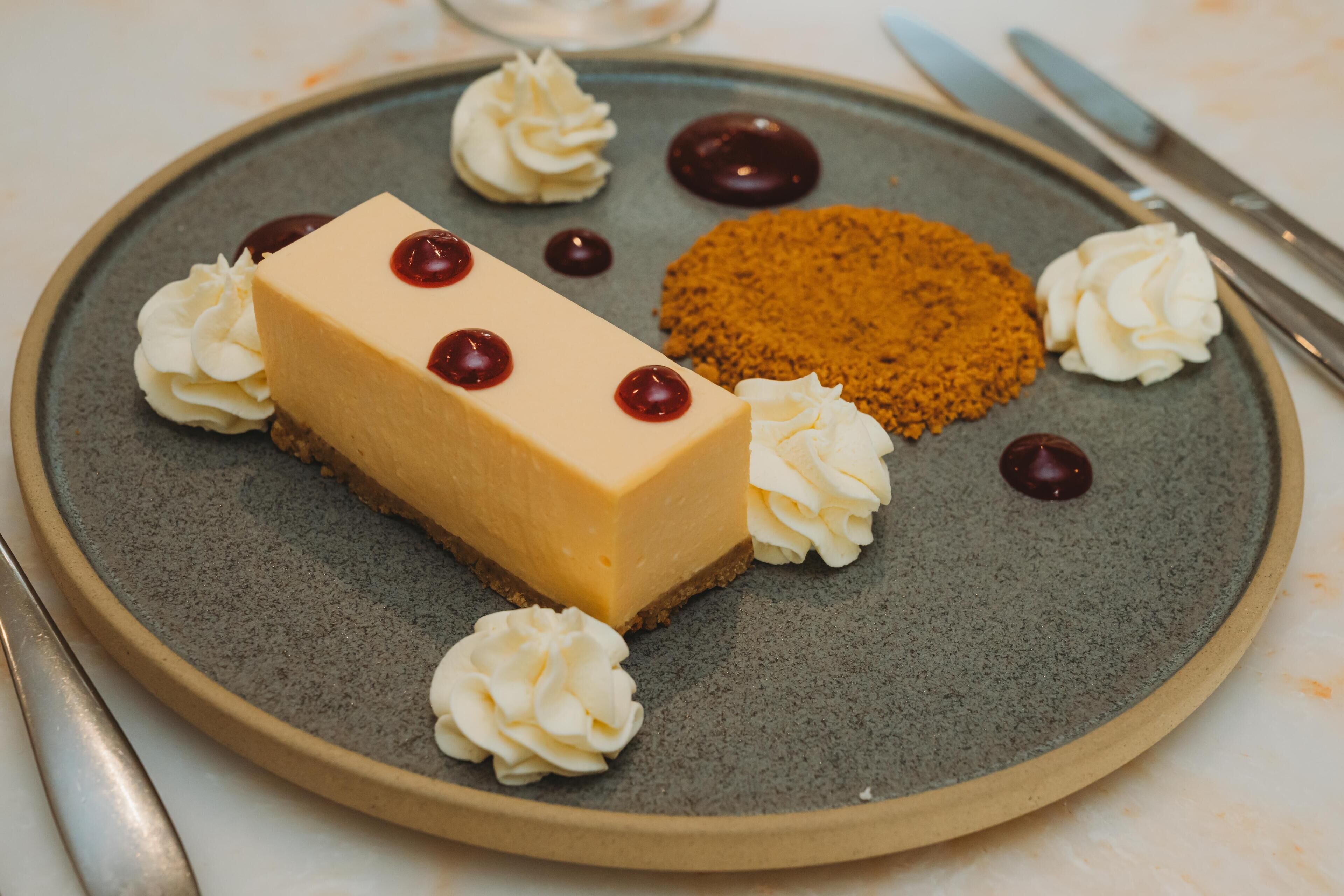 Un plato con postre, un pastel de queso, crema batida y migas de chocolate.