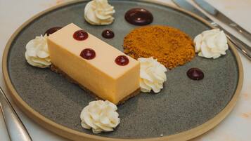 Un plato con postre, un pastel de queso, crema batida y migas de chocolate.