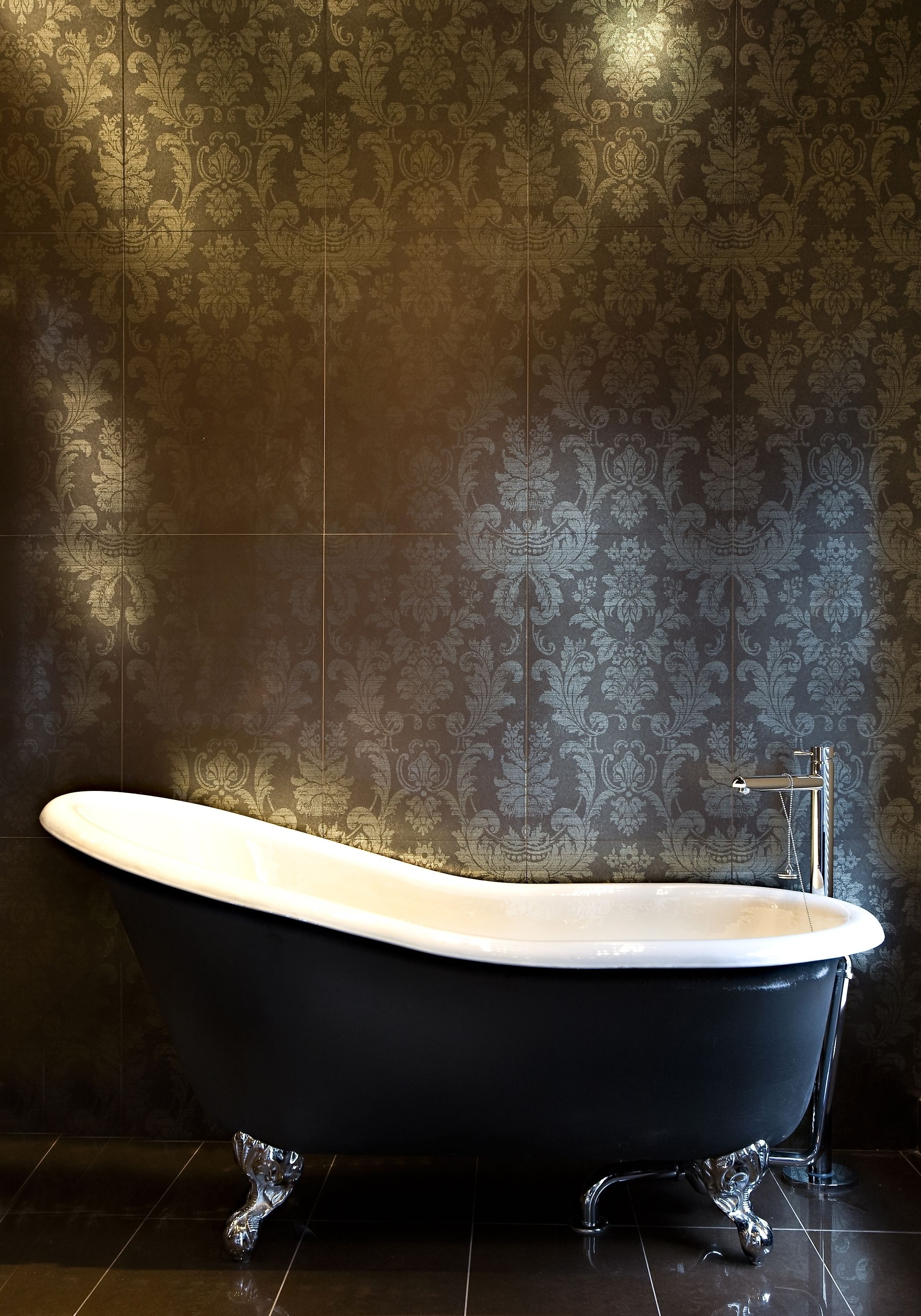 A black freestanding bathtub in a bathroom with a patterned wallpaper background.
