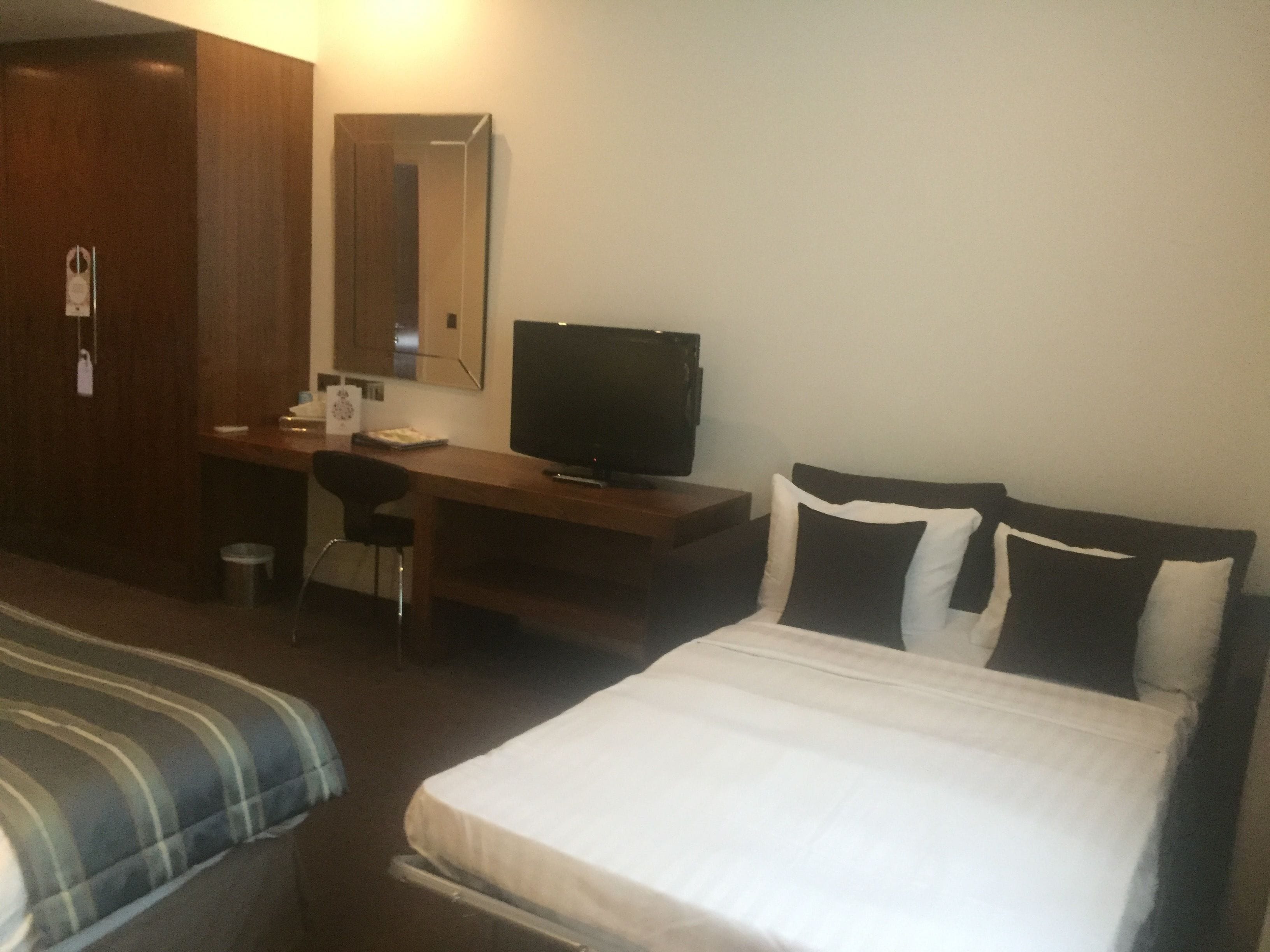 A hotel room with a bed, a desk with a chair, a television, and a wardrobe.