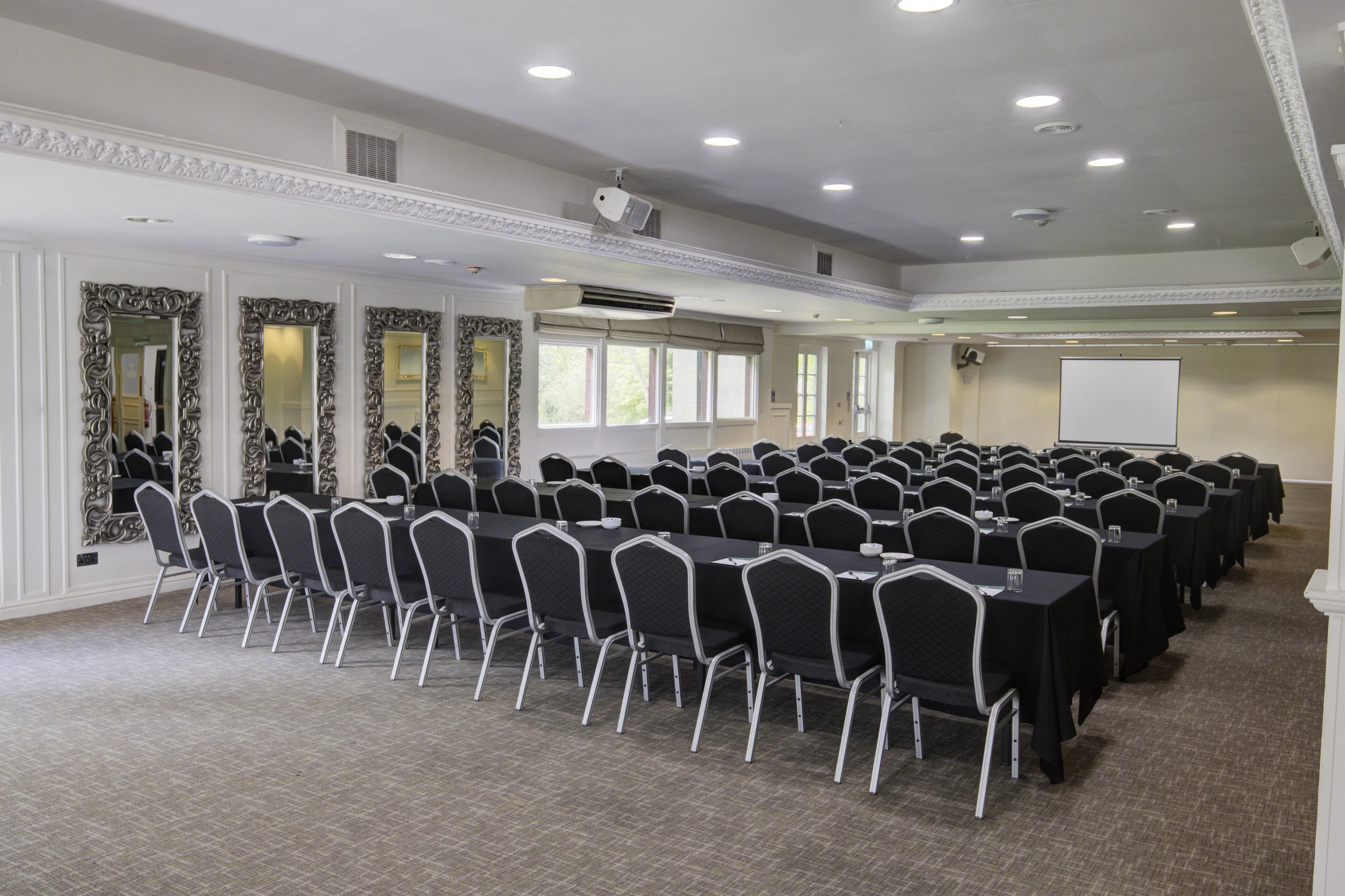 A conference room with rows of tables and chairs, a whiteboard, and a projector screen.