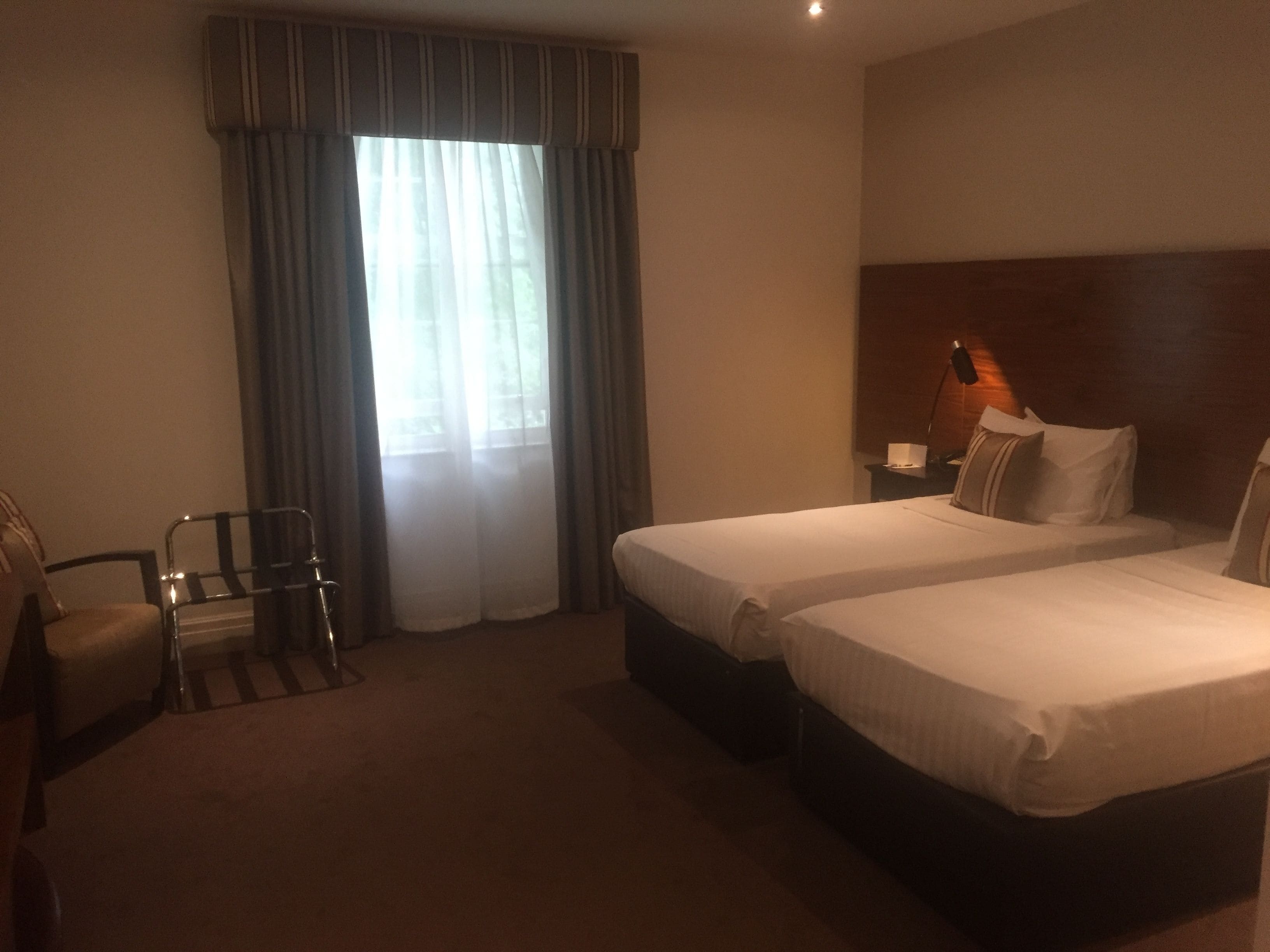 A hotel room with two beds, a chair, a nightstand, and a lamp.