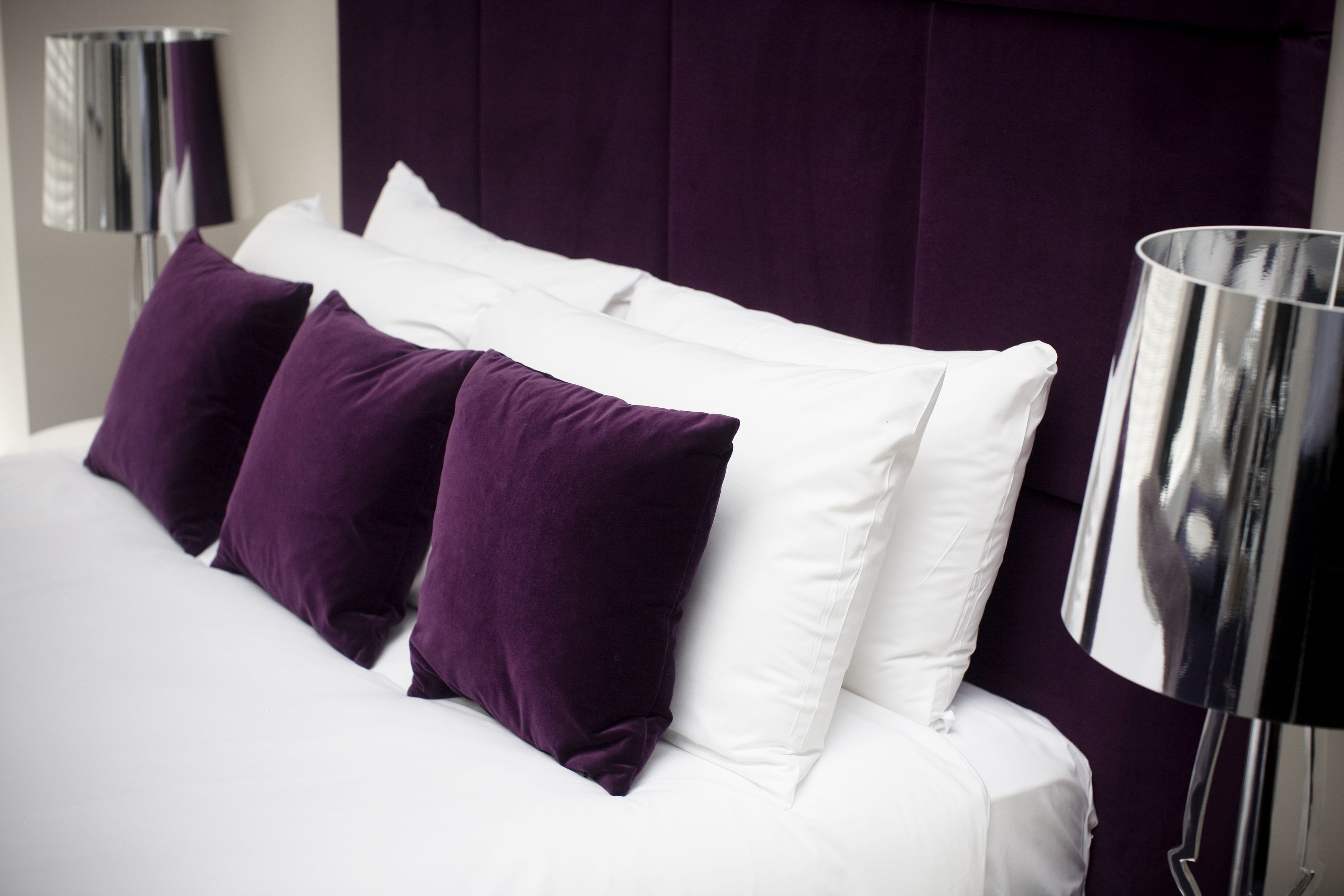A bed with white and purple bedding, a dark headboard, and a modern floor lamp.