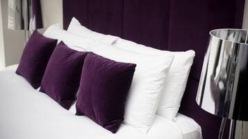 A bed with white and purple bedding, a dark headboard, and a modern floor lamp.