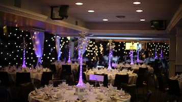 Un salón de banquetes con mesas redondas dispuestas para un evento formal, con centros de mesa iluminados y una iluminación ambiental tenue.