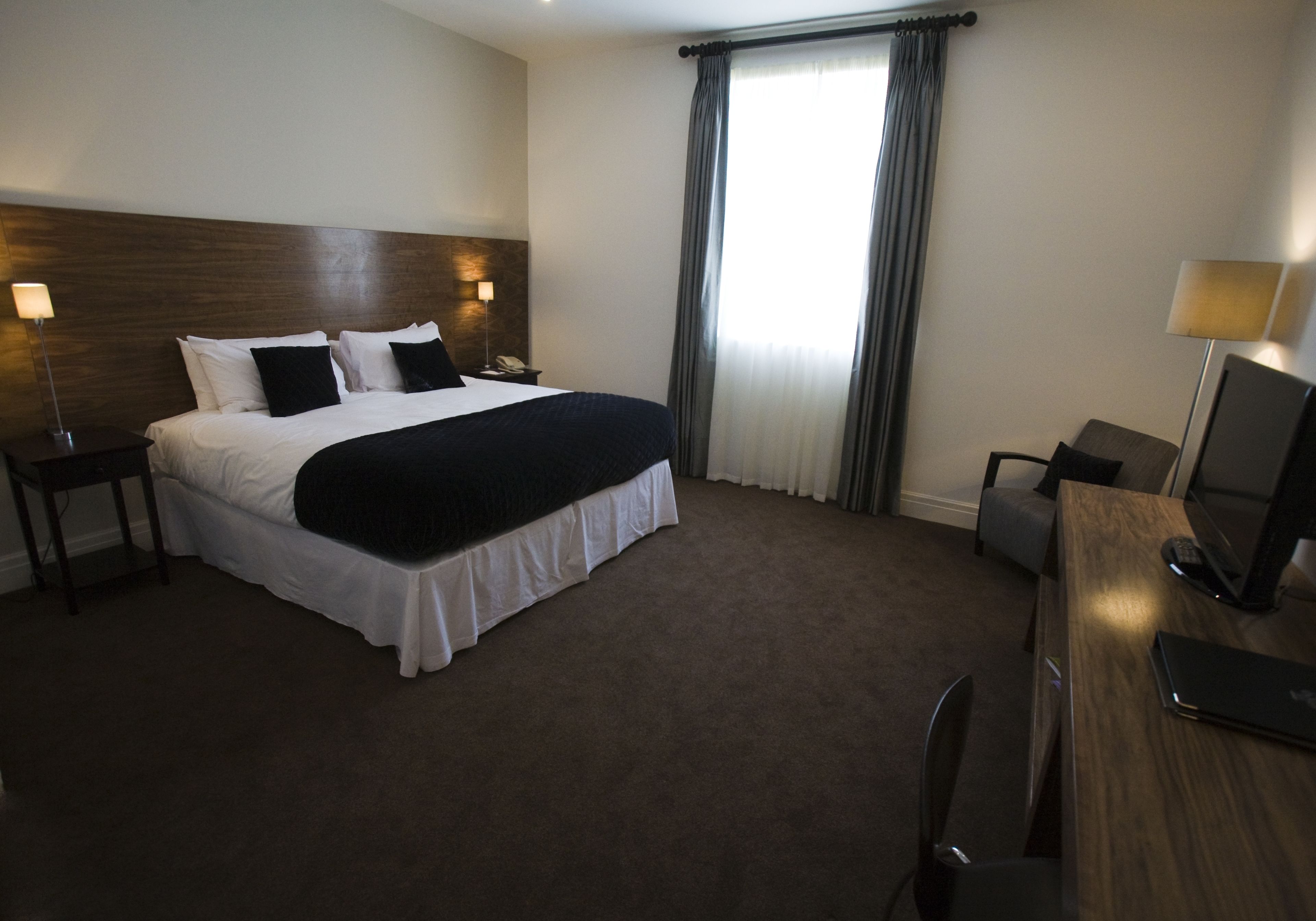 A hotel room with a large bed, a desk with a chair, a desk lamp, and a flat-screen TV.