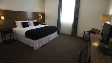 A hotel room with a large bed, a desk with a chair, a desk lamp, and a flat-screen TV.