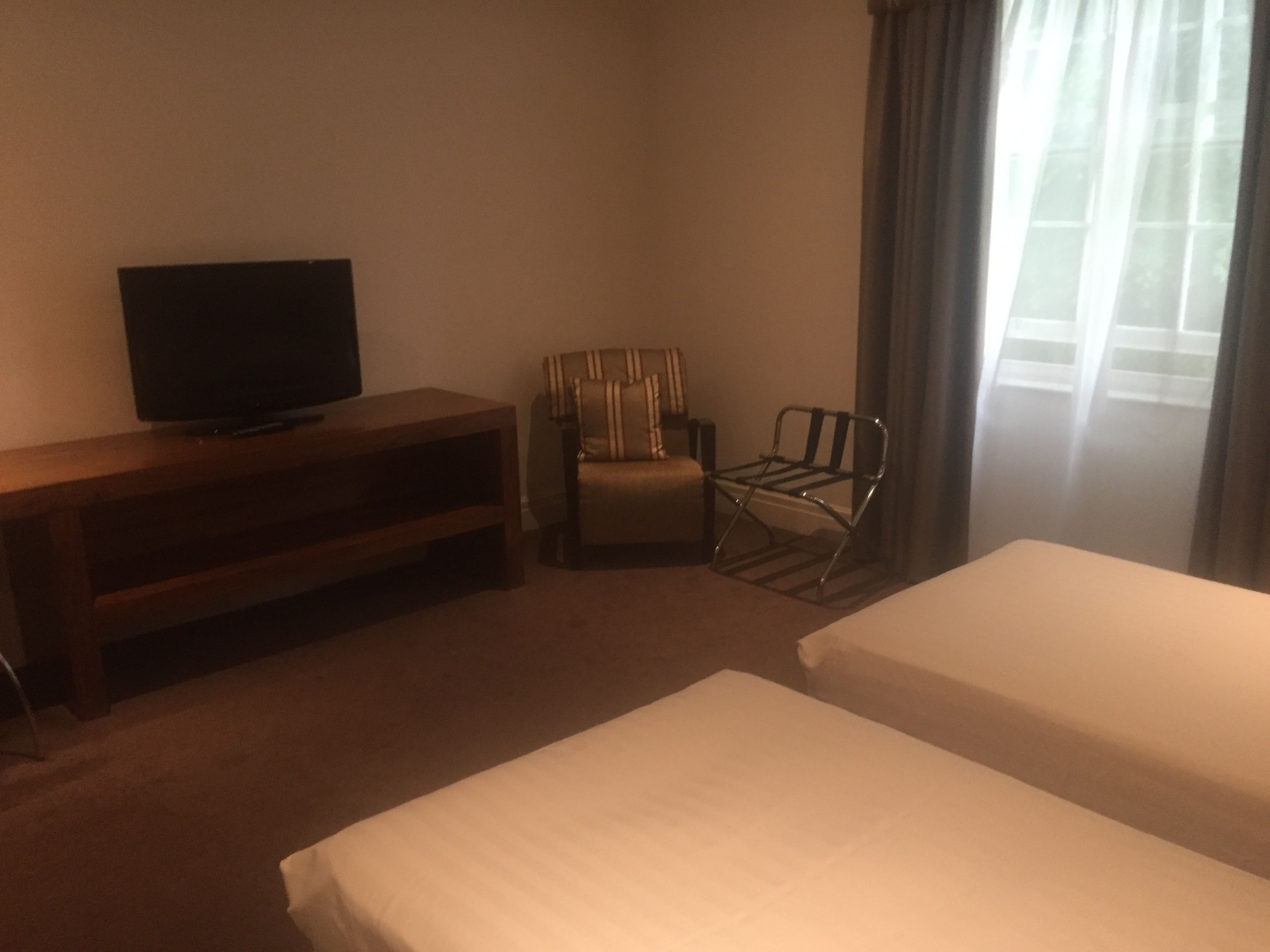 A hotel room with two beds, a TV on a wooden stand, a striped armchair, and a metal chair.