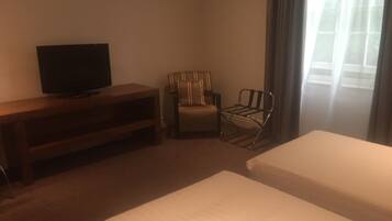 A hotel room with two beds, a TV on a wooden stand, a striped armchair, and a metal chair.