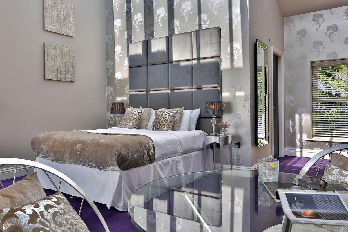 A modern bedroom with a large bed, bedside lamps, a glass coffee table, and a view of the outdoors.