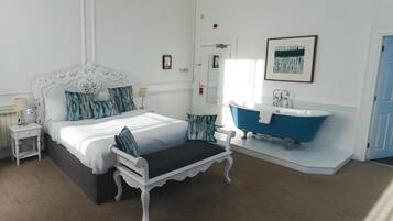 A bedroom with a large bed, a nightstand, a vanity with a blue bathtub, and a door with a mirror.