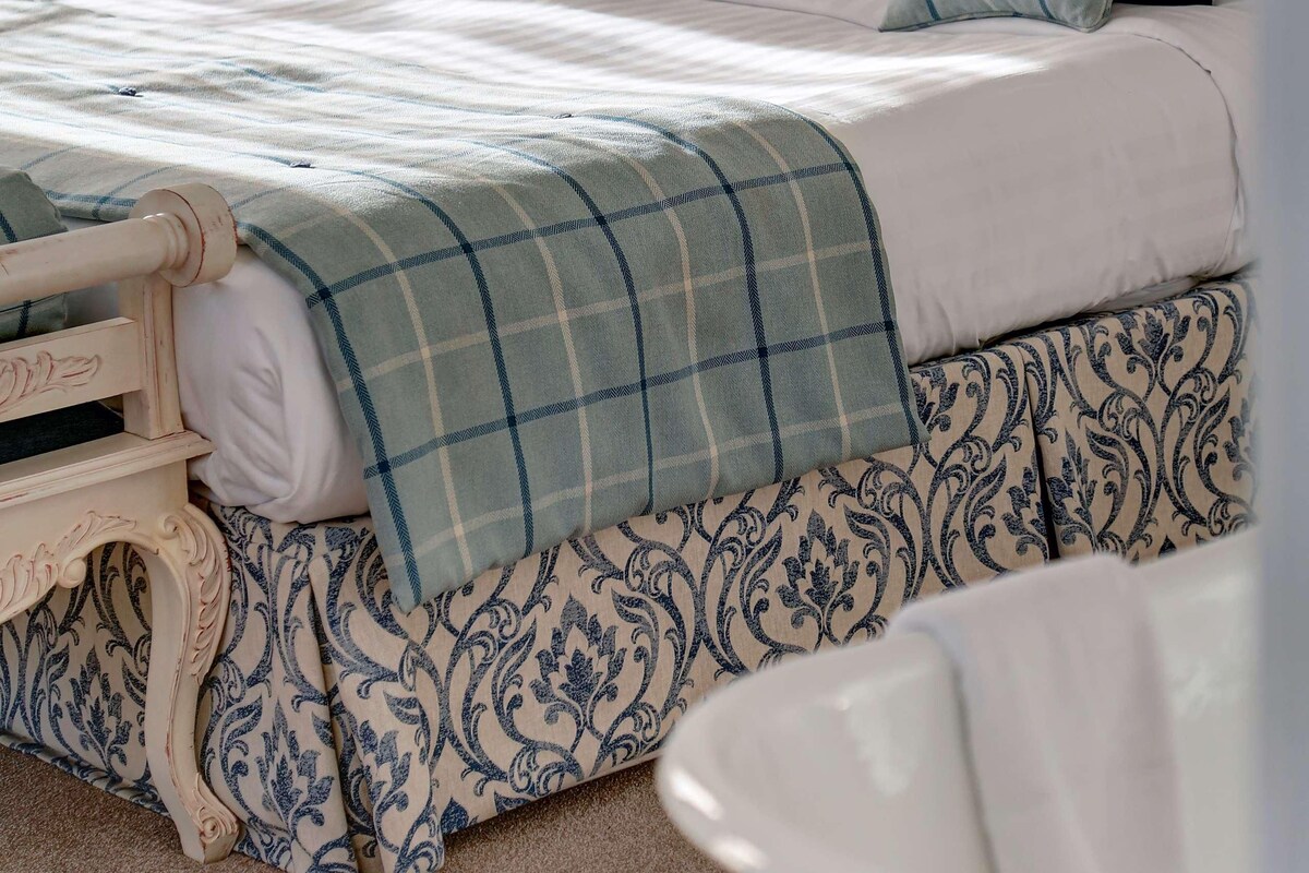 A neatly made bed with a plaid bedspread, a decorative headboard, and a bedside table with a lamp.