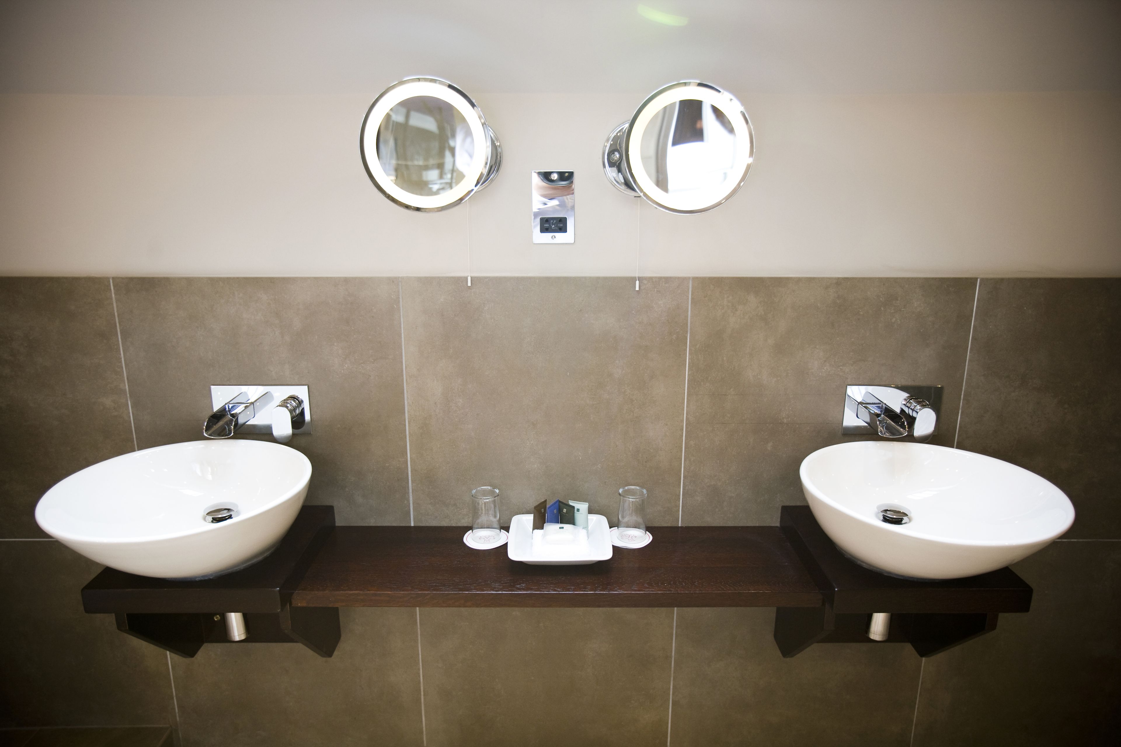 Een badkamer met twee wastafels, elk met een spiegel erboven, en een klein schapje met toiletartikelen.