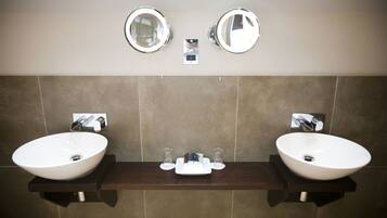 A bathroom with two sinks, a mirror above each, and a small shelf with toiletries.