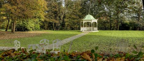 A gazebo in a park with a pathway leading to it, surrounded by trees and benches.