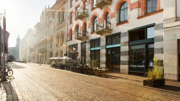 Eine Kopfsteinpflasterstraße gesäumt von historischen Gebäuden, mit Außenplätzen für Cafés und freiem Blick in den Himmel.