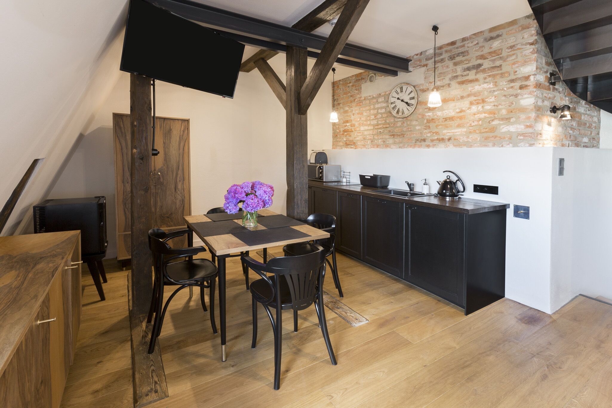 A modern kitchen with a brick wall, wooden flooring, and a dining area with a table and chairs.