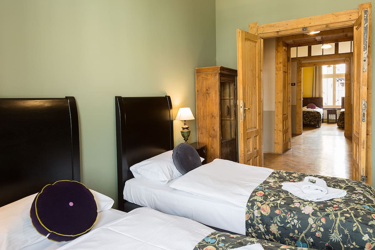 Habitación de hotel con dos camas, un armario de madera y un pasillo que da a otra habitación.