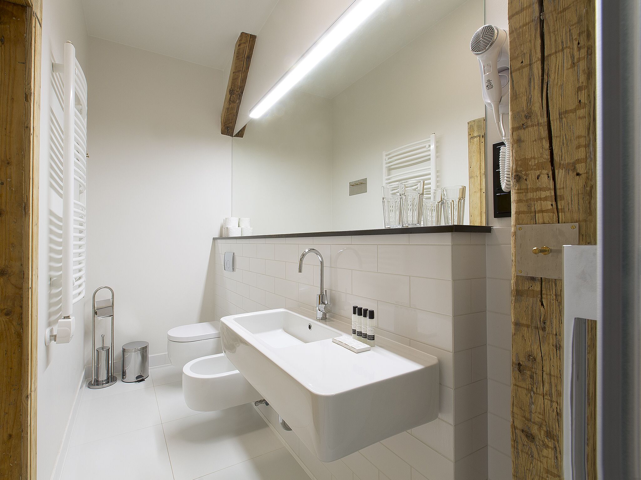 Ein modernes Badezimmer mit einem weißen Waschbecken, zwei Toiletten und einer Wand mit Holzverkleidung.