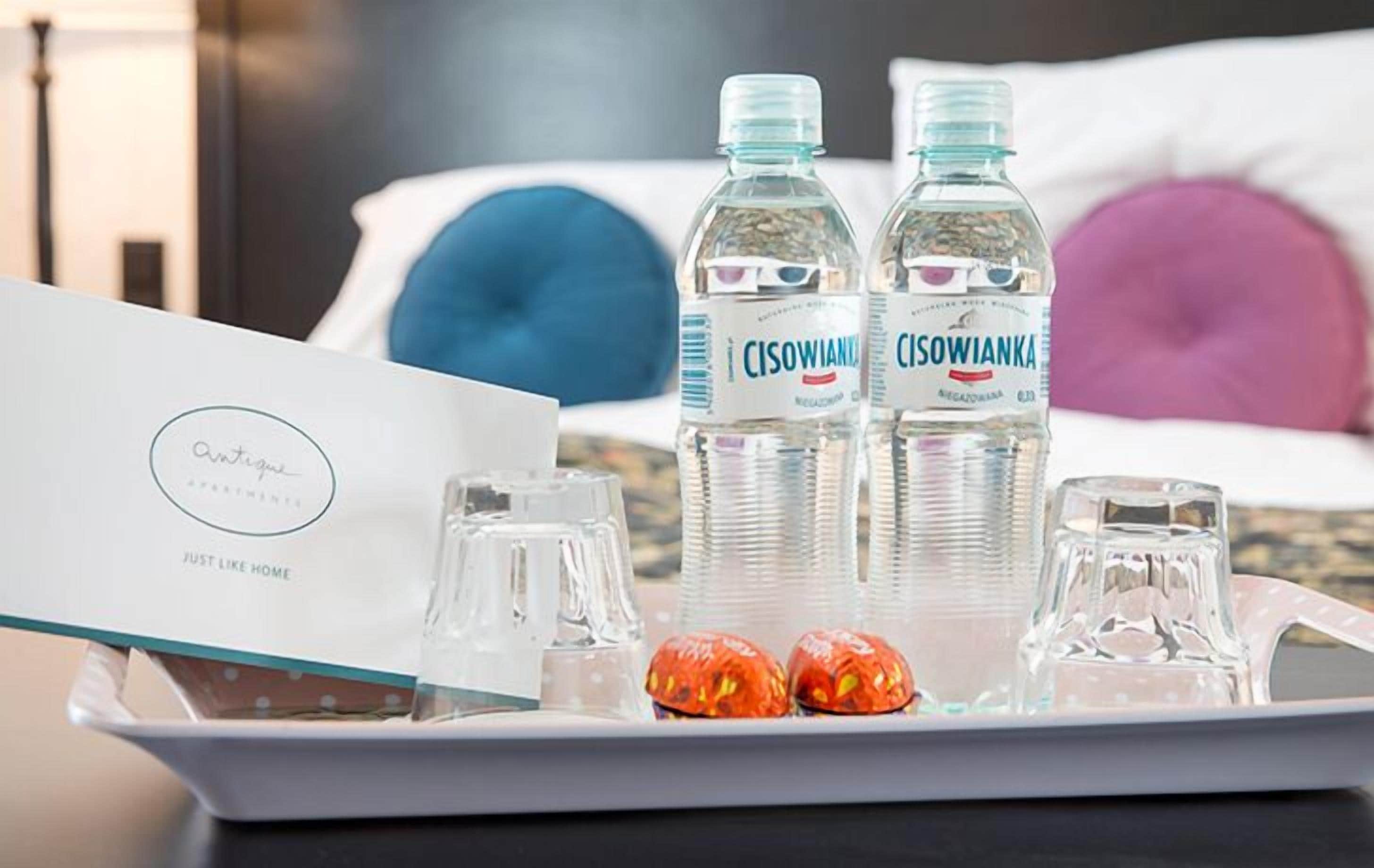 A tray with two bottles of water, a glass, and two small red items on a hotel room table.