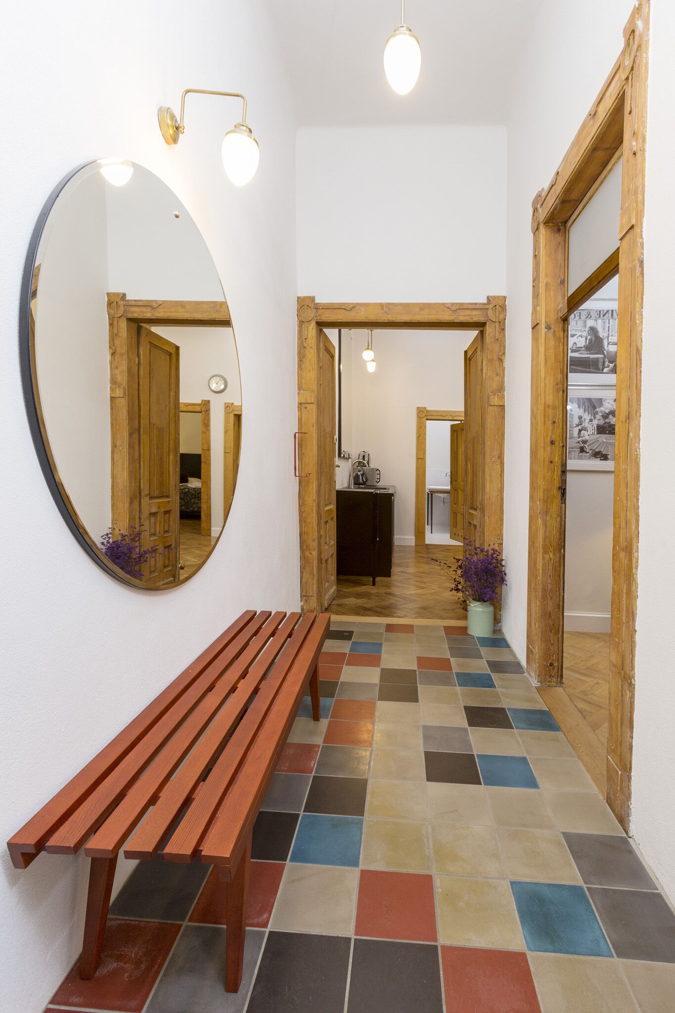 A hallway with a wooden bench, a large mirror, and a tiled floor.