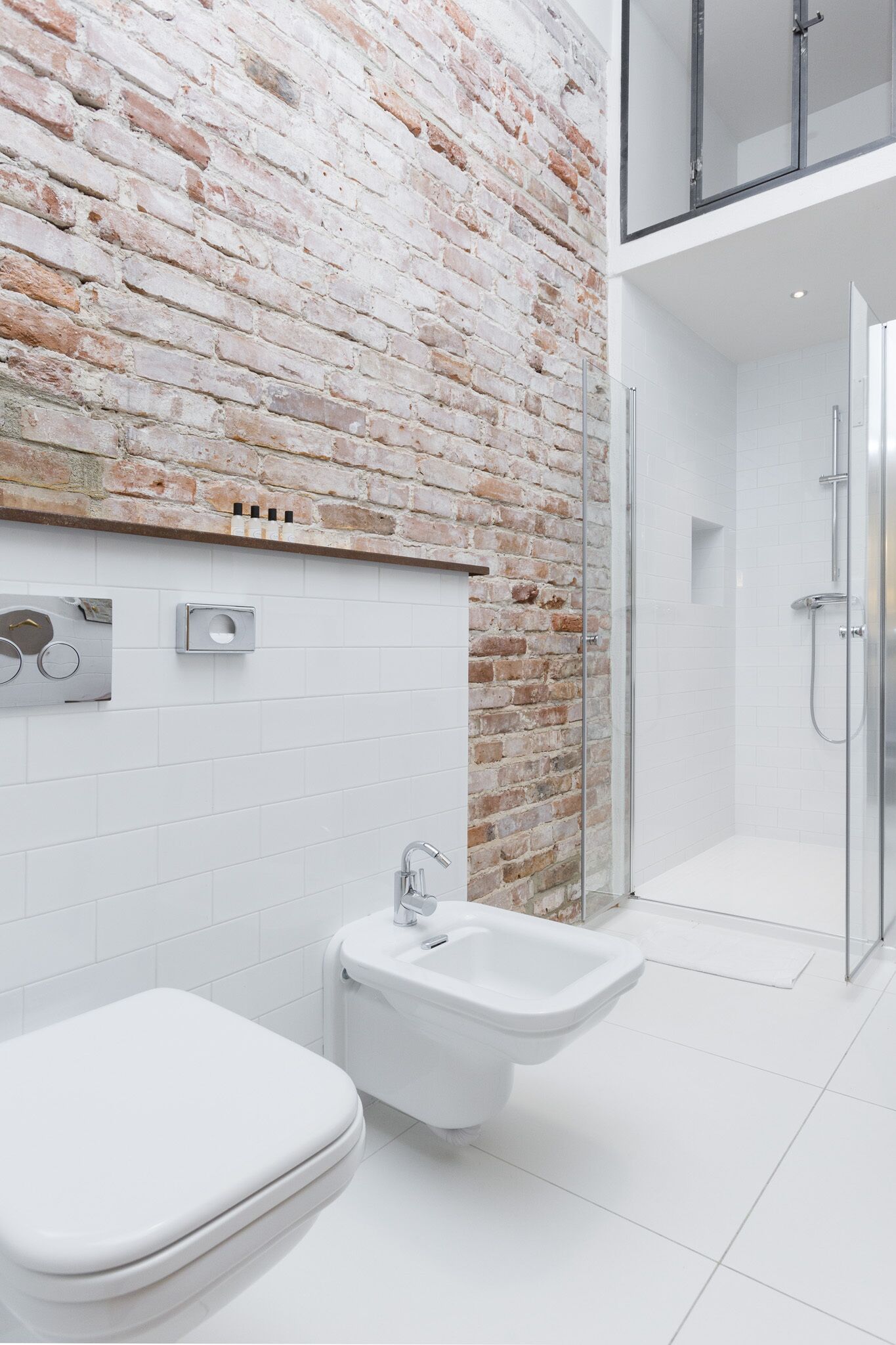 A modern bathroom with a brick wall, a toilet, a bidet, and a glass-enclosed shower.