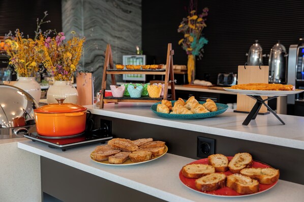 Un bufé de desayuno con diversos pasteles, pan y una olla caliente sobre una encimera de cocina moderna.