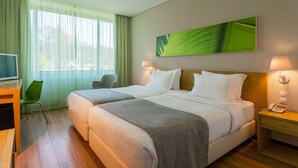 A hotel room with two beds, a desk, a chair, and a large window with sheer curtains. - HF Fénix Garden (Lisbon)