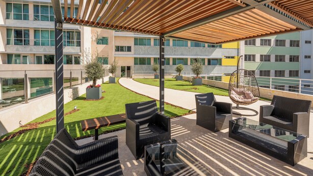 An outdoor seating area with wicker furniture and a hanging chair, overlooking a landscaped garden and a building complex. - HF Fénix Garden (Lisbon)