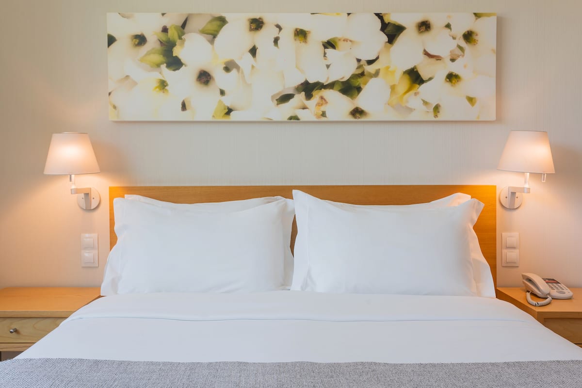 Una cama bien tendida con sábanas blancas, dos lámparas de noche y un teléfono en la mesita.