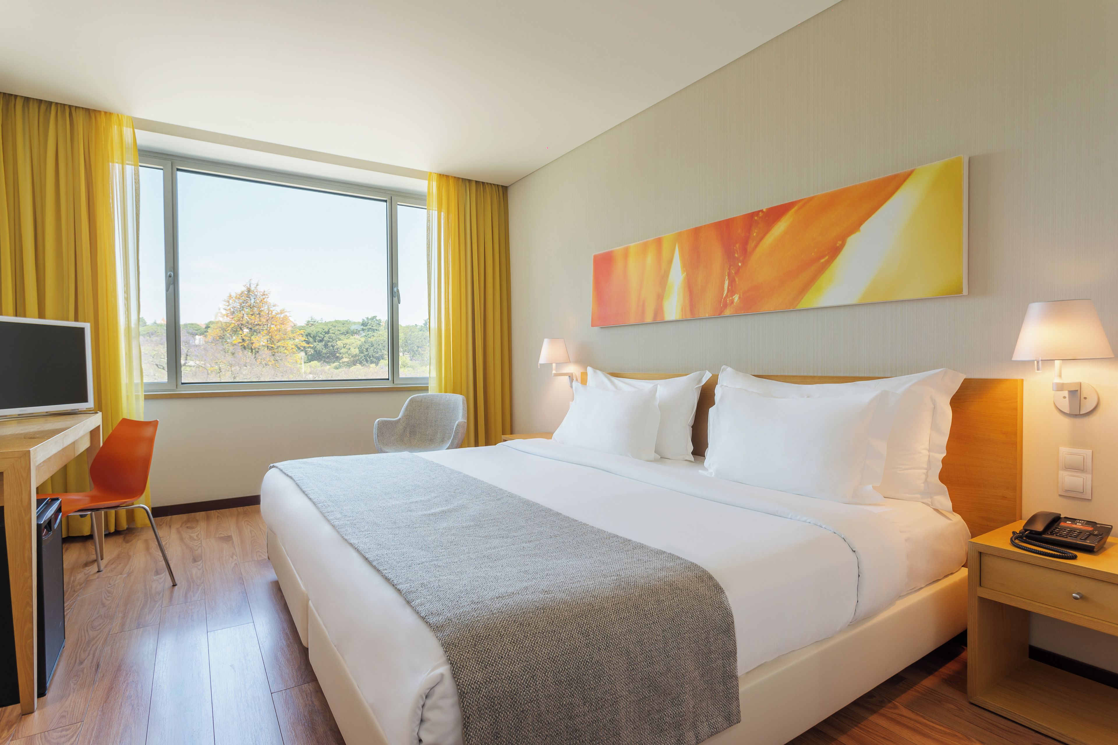 A hotel room with a bed, bedside lamps, a desk with a chair, a television, and a window with curtains.