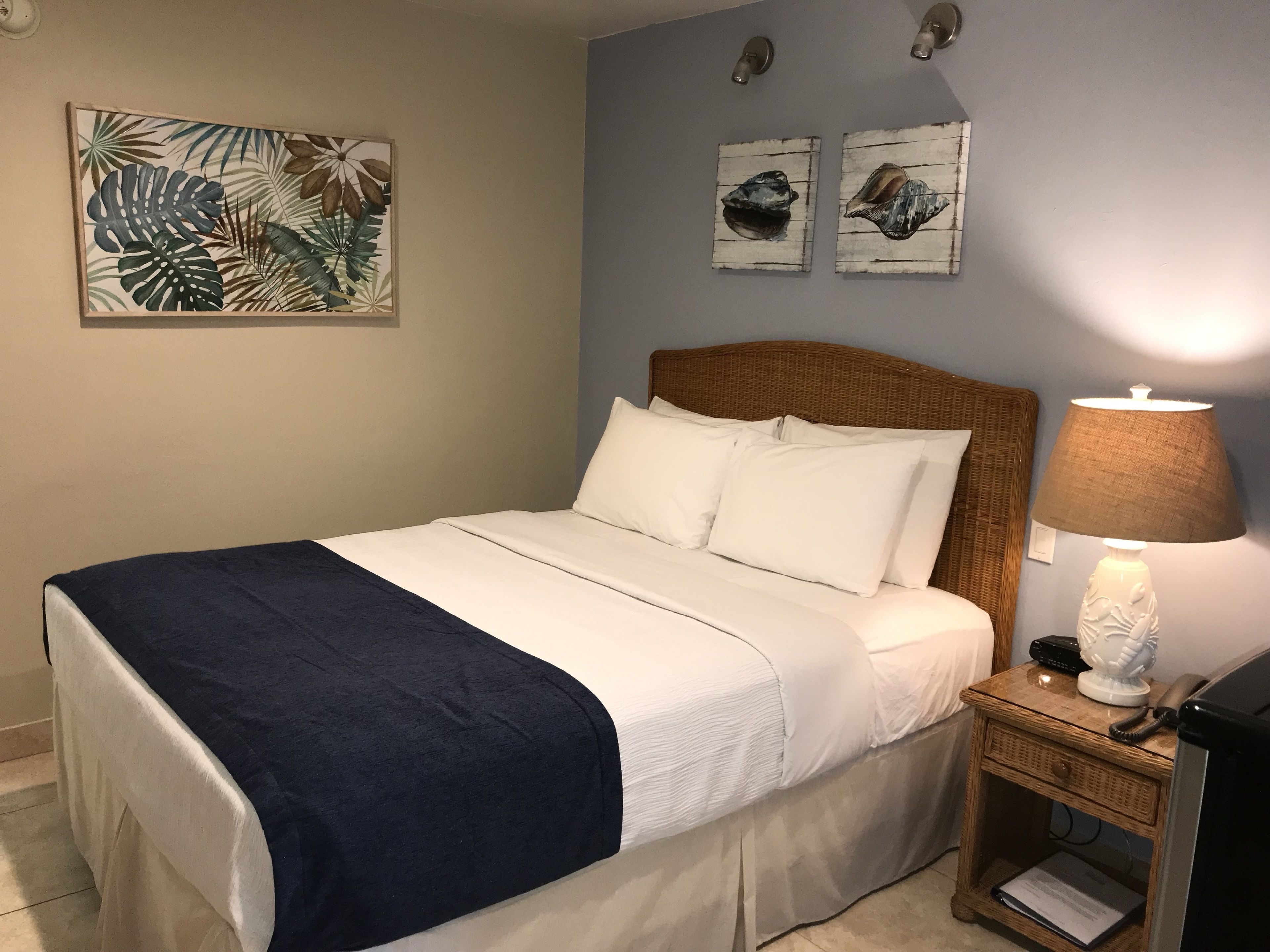 A neatly made bed with white and navy bedding, a wooden headboard, and a bedside lamp.