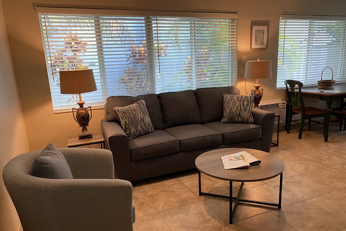 A living room with a sofa, armchair, coffee table, and a dining table with chairs.