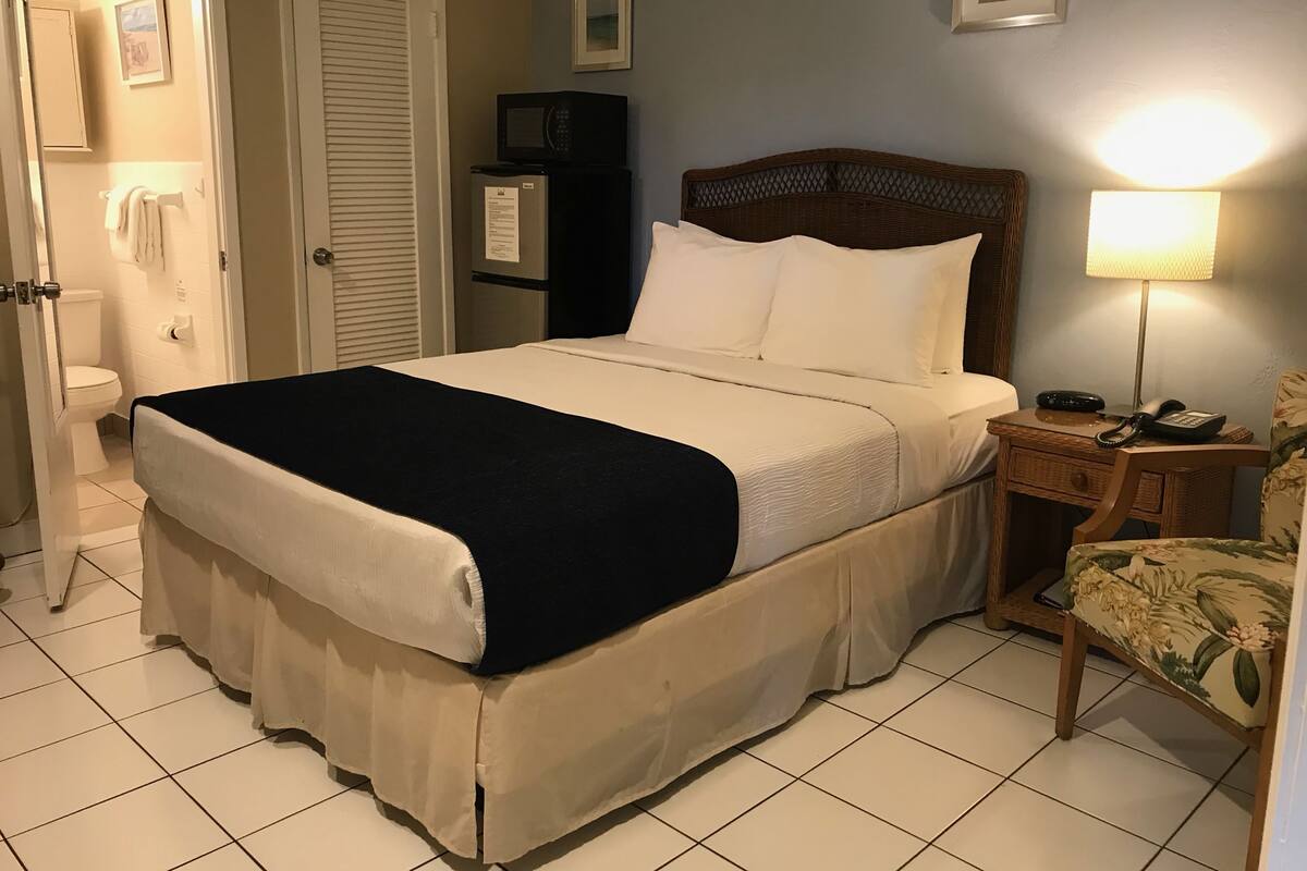 A hotel room with a bed, a bedside table with a lamp, a chair, a wardrobe, a toilet, and a picture on the wall.