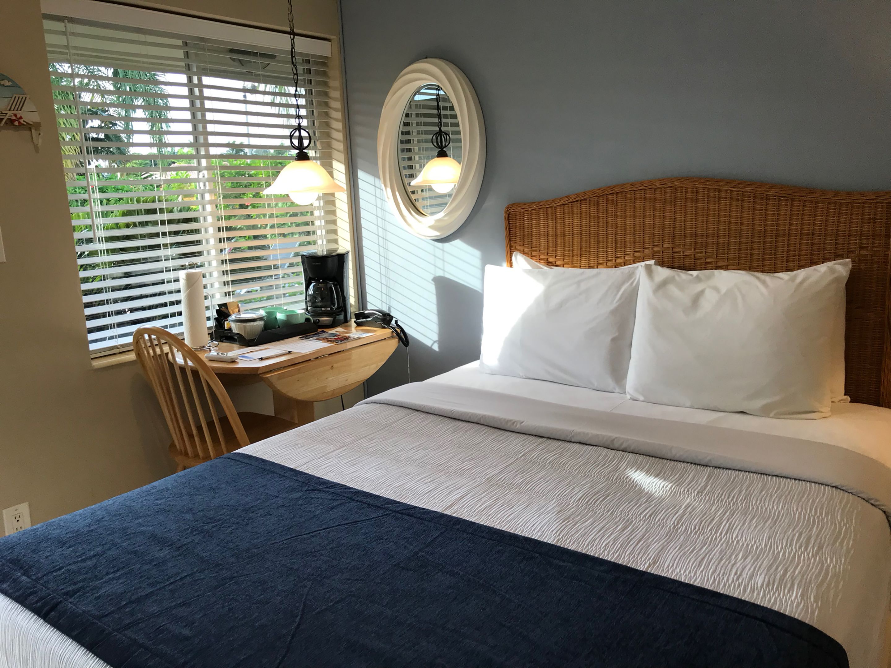 Een slaapkamer met een bed, een bureau met koffiezetapparaat en een raam met jaloezieën.