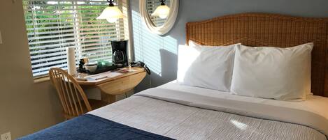 Een slaapkamer met een bed, een bureau met koffiezetapparaat en een raam met jaloezieën.