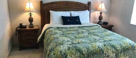 A neatly made bed with a floral bedspread, two bedside lamps, a wooden nightstand with a telephone, and two framed pictures on the wall.