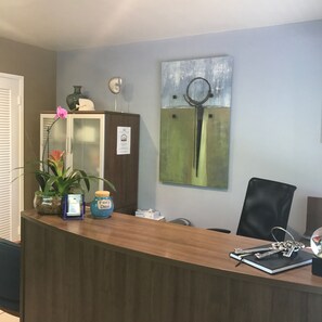 A reception desk with a wooden counter, a potted plant, a vase, and a decorative item labeled 'Fairy Dust'. - Casitas Coral Ridge (Fort Lauderdale)