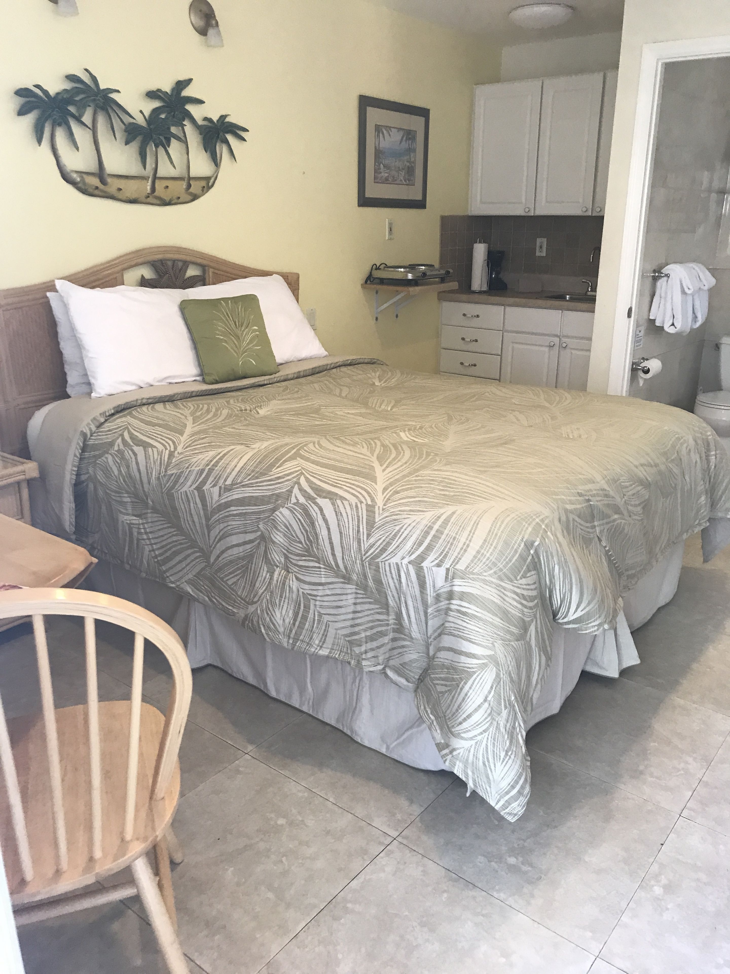 Un dormitorio con cama, una silla, una mesita, una zona de cocina y un baño.